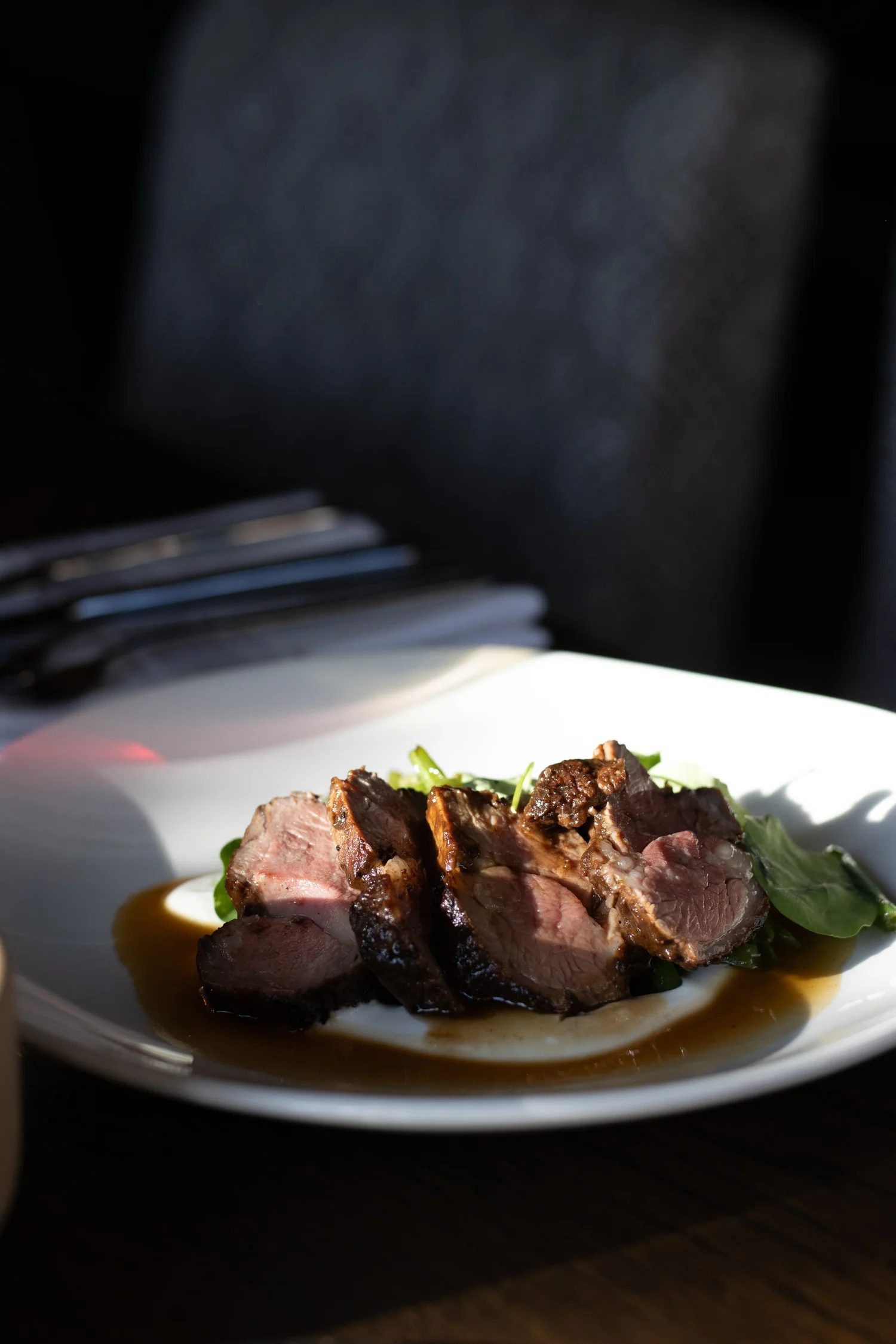 Close-up of a plated gourmet steak dish with sliced beef, greens, and sauce, on a white plate. The Lamb Inn. 