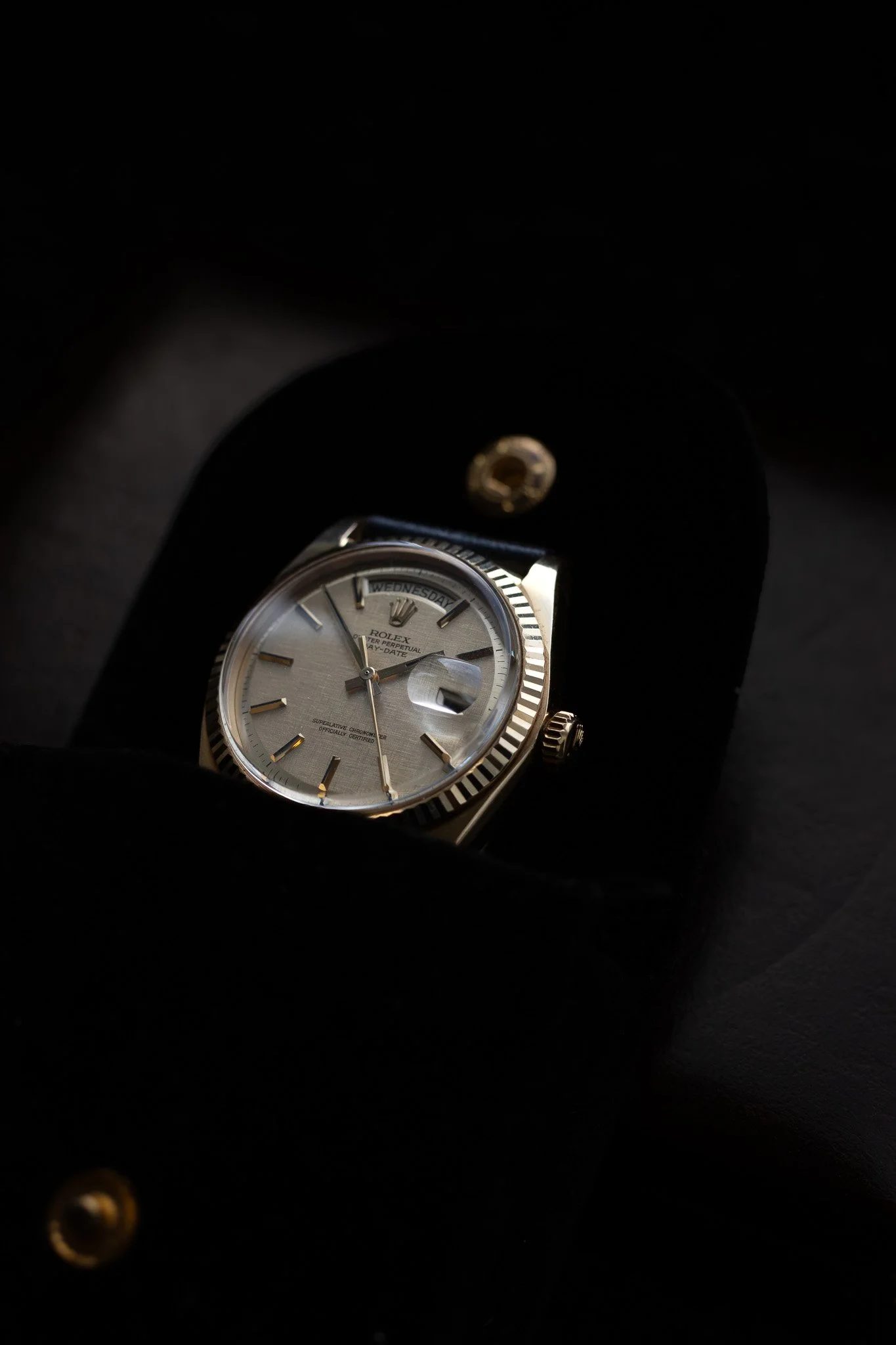 Close-up of a Rolex watch with a silver face and gold accents, displayed inside a black box with a folded lid. Aurmont. Watches.