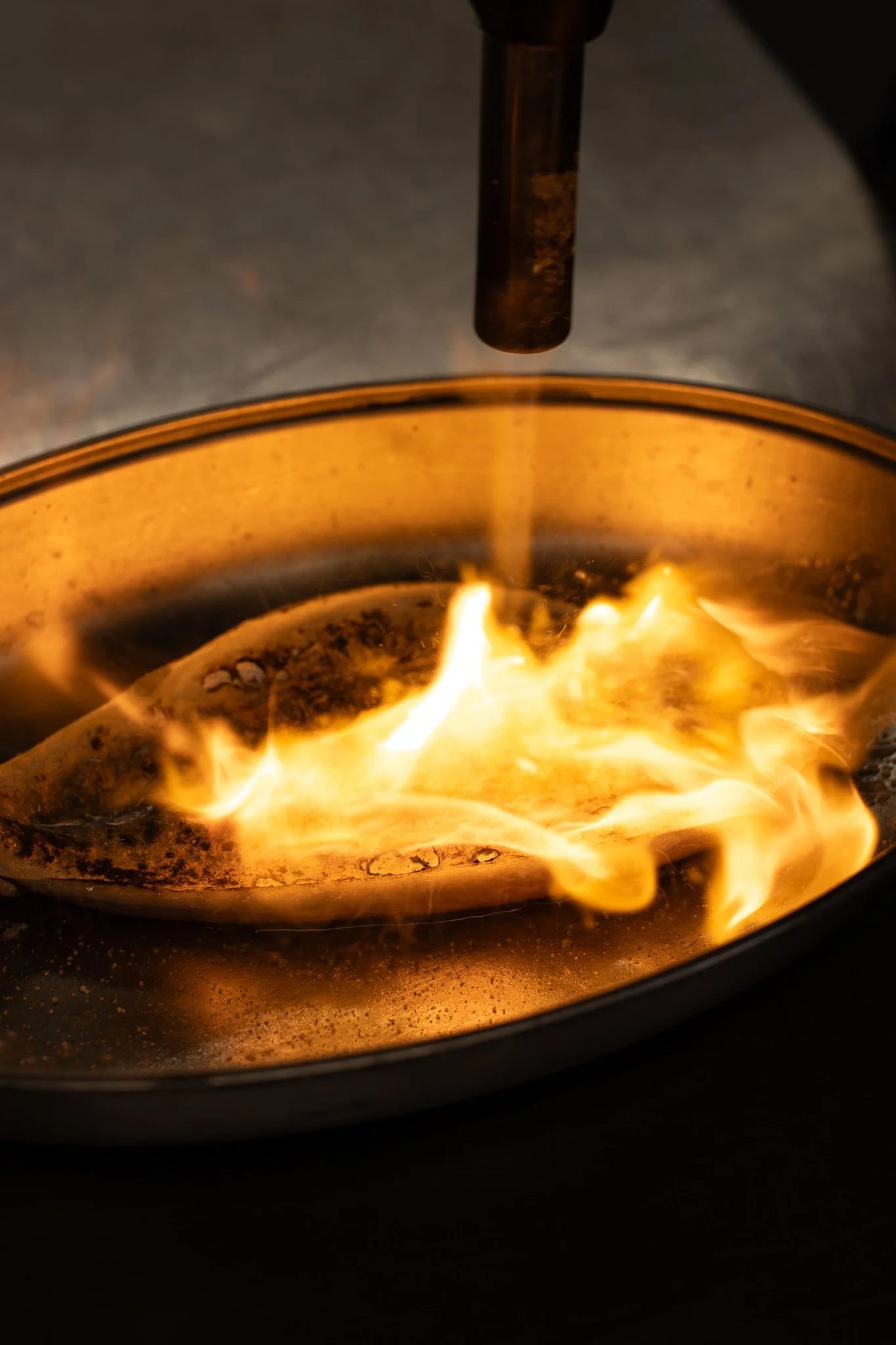 A close-up of a wood-burning stove with a visible flame and a metallic pipe above it. The Lamb Inn. 