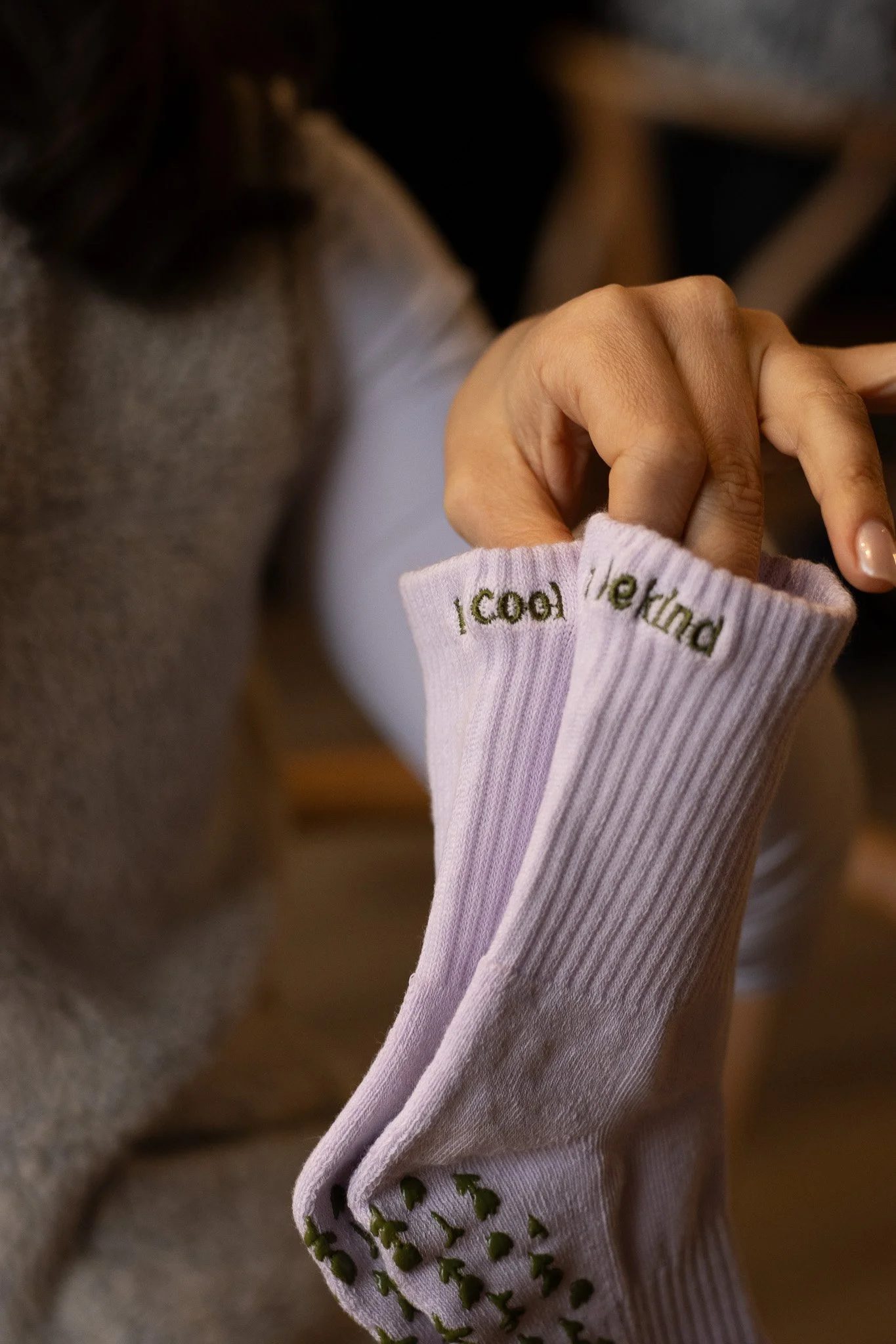 Close-up of a woman's hand with a pink long-sleeve shirt featuring embroidered green text and designs. She is touching her face with the other hand, and her brown hair is partially visible. GetAGrip Apparel.