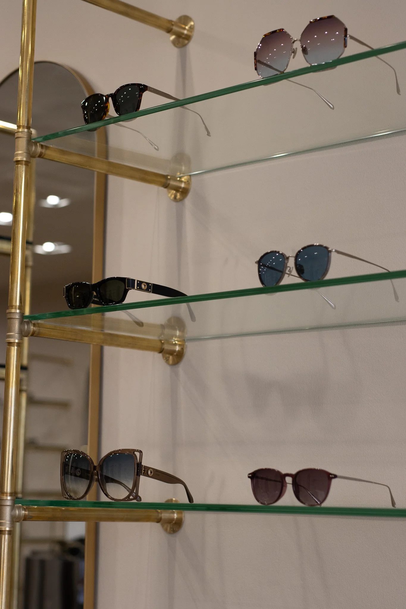 Display of sunglasses on glass shelves with gold-colored metal frame. Linda Farrow.