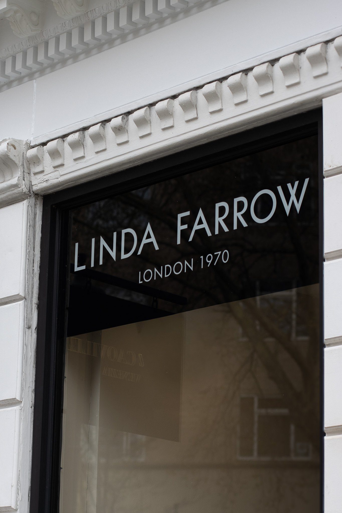 Close-up of a shop window with white lettering that reads 'LINDA FARROW LONDON 1970'. The architectural details include decorative molding on the building's corner. Linda Farrow.