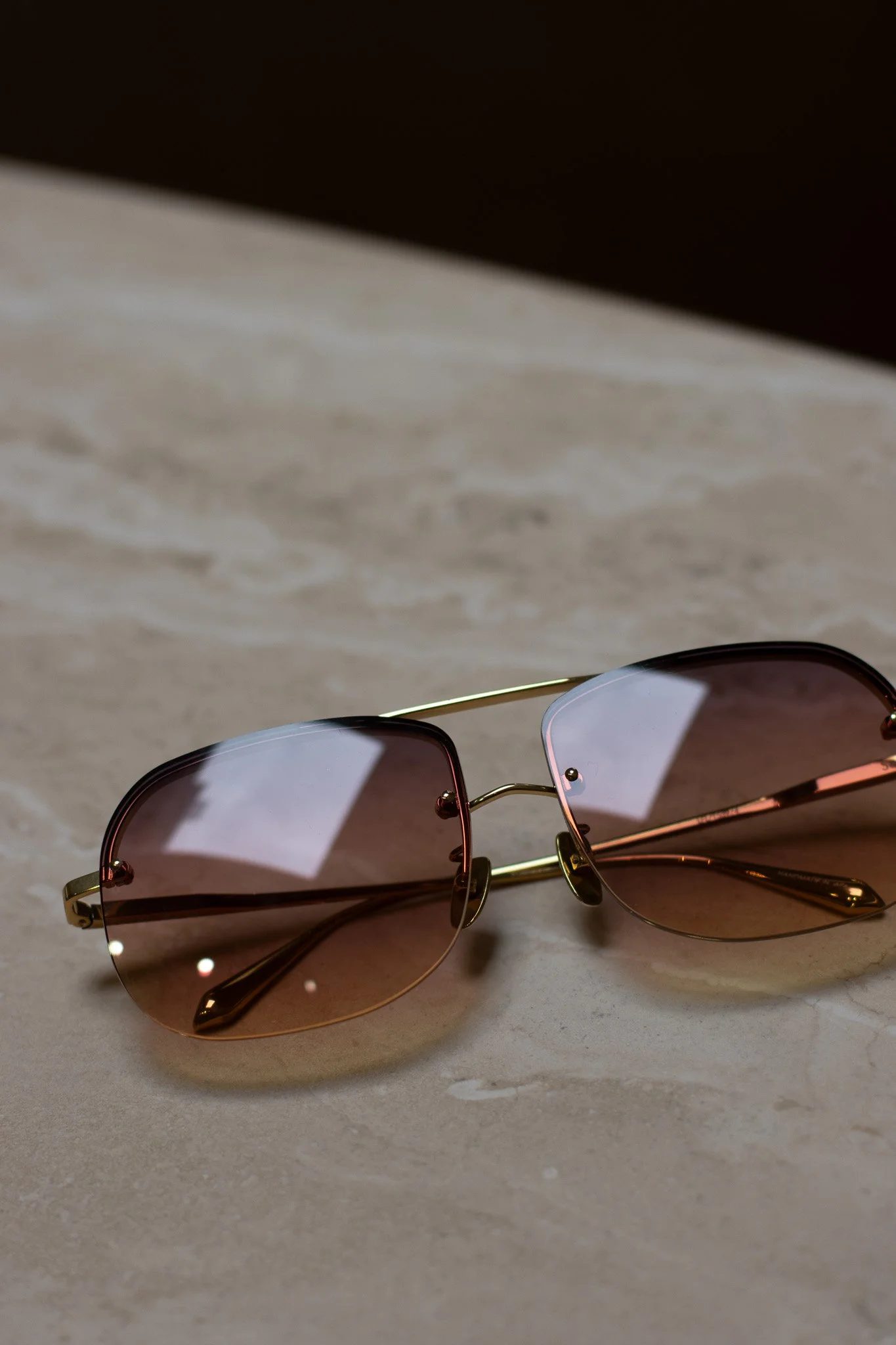 A pair of sunglasses with rose gold frames and tinted lenses resting on a white surface. Linda Farrow.